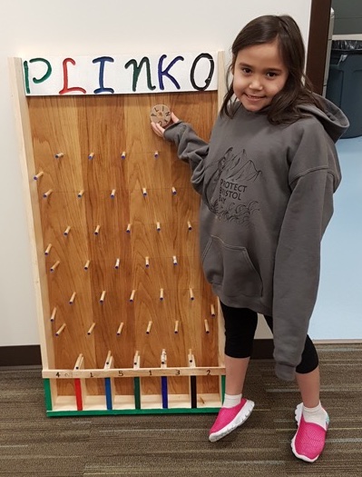 A student poses in front of a homemade plinko board.