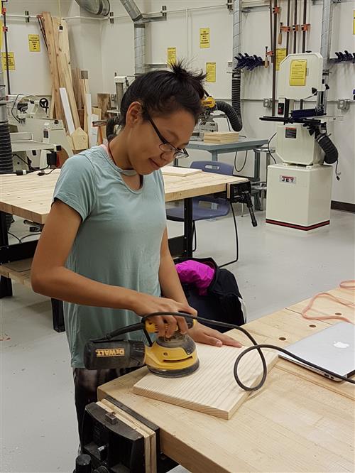 Student using a disc sander to prepare wood for burning.  