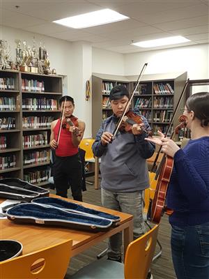 Teacher instructing 2 boys playing the violin  